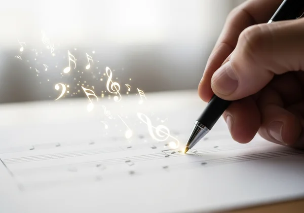 Eine Hand schreibt Musiknoten auf leeres Notenpapier