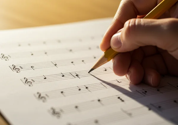 Hand writing notes on blank staff paper with a pencil
